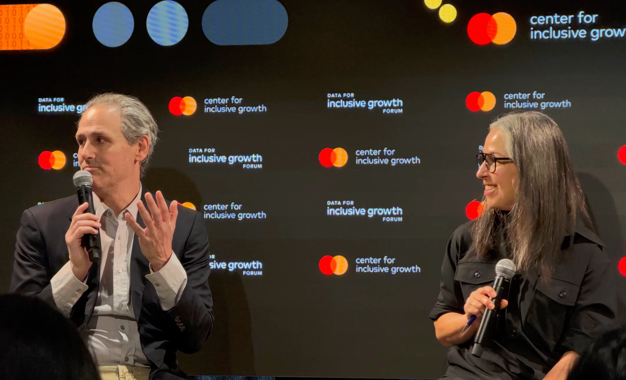 Two speakers holding microphones during a panel at the Data for Inclusive Growth Forum.