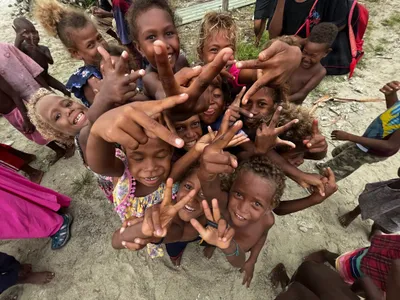 Children crowd together and wave toward the camera.