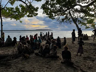 A group gathers beneath a tree beside the sea.