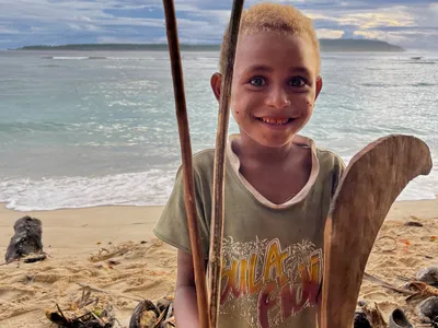 A child holds a wooden paddle beside the beach.