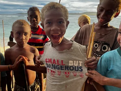 Children pose together on the beach with wooden paddles.