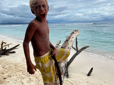 A smiling child holds a wooden paddle beside the sea.