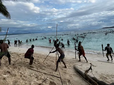 Participants carrying poles run into the shallow sea.