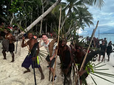 Participants carrying poles pose together beneath the palms.