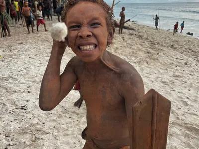 A child makes a playful face beside the sea.