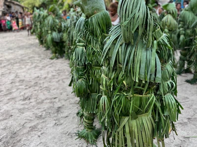 Participants wear dense green leaf coverings on a sandy path.