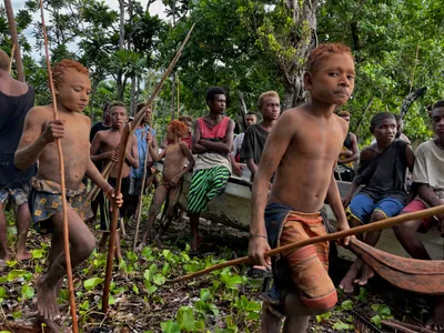 A child holding a pole stands in front of a beachside group.