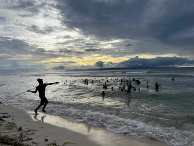 Participants gather in shallow water beneath dramatic clouds.