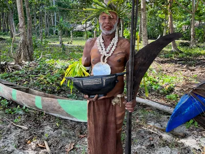 A participant wearing shells and leaves holds a wooden paddle.
