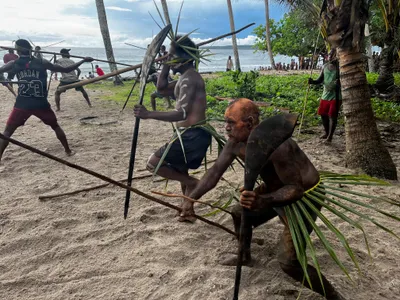 Participants hold long poles on a sandy beach.