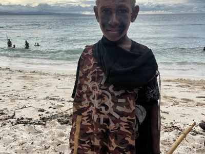 A child with painted face poses beside the sea.