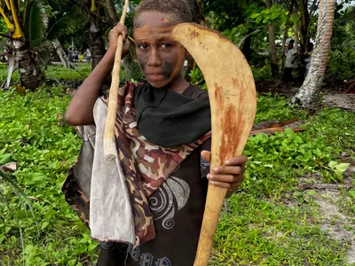 A child stands beneath the palms with a wooden paddle.