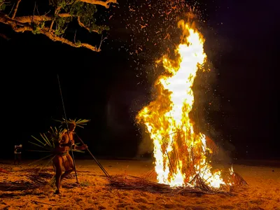 Participants with poles surround a nighttime bonfire.