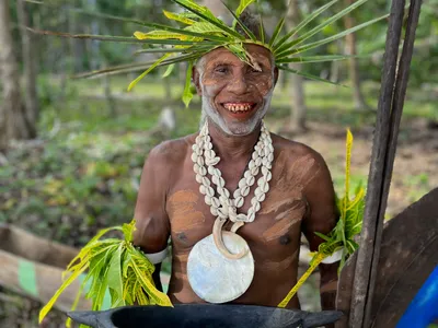 A smiling participant wears shells, body paint, and a leaf headdress.