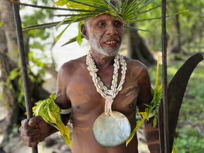 A participant wearing shell necklaces holds a wooden paddle.